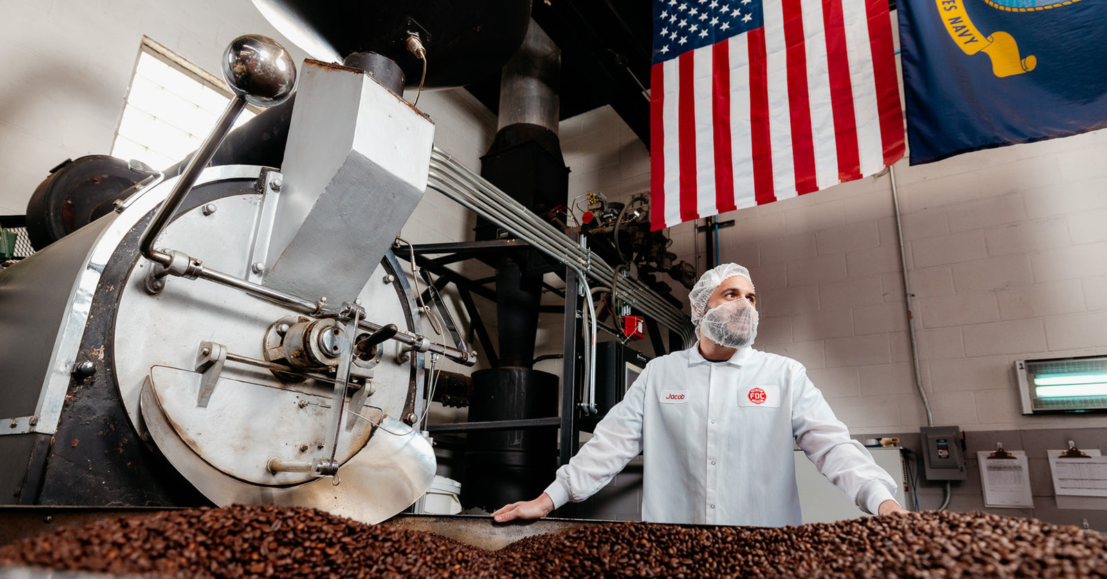 Jake Ball, Fire Dept. Coffee's Director of Coffee, standing behind a coffee roaster wearing a lab coat.