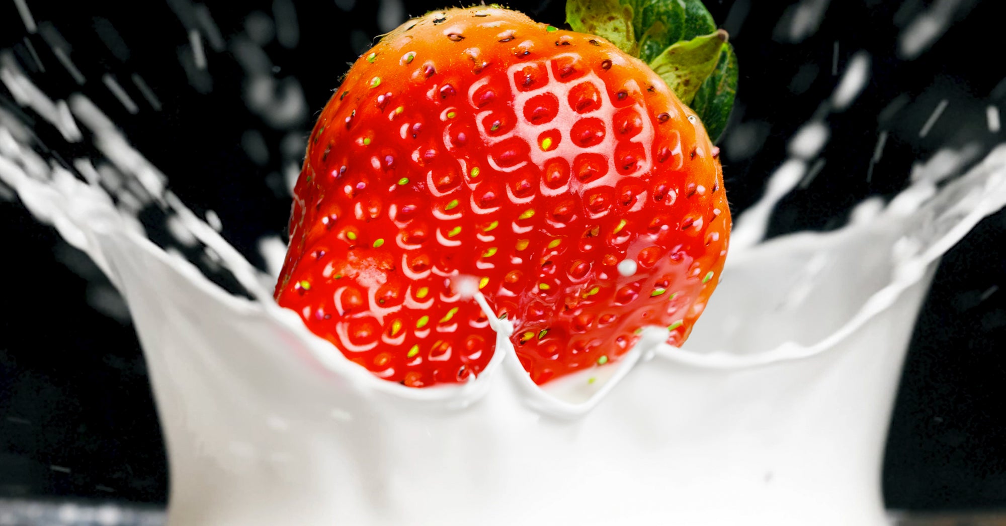 Strawberry splashing into a bowl of cream.