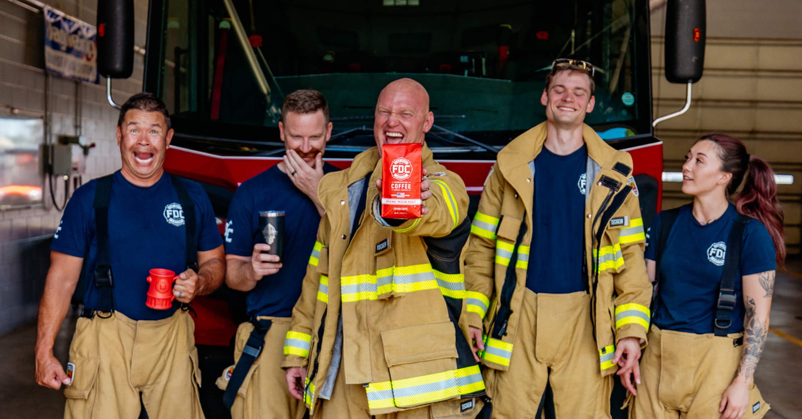The Fire Department Coffee video team laughing together in front of a firetruck.