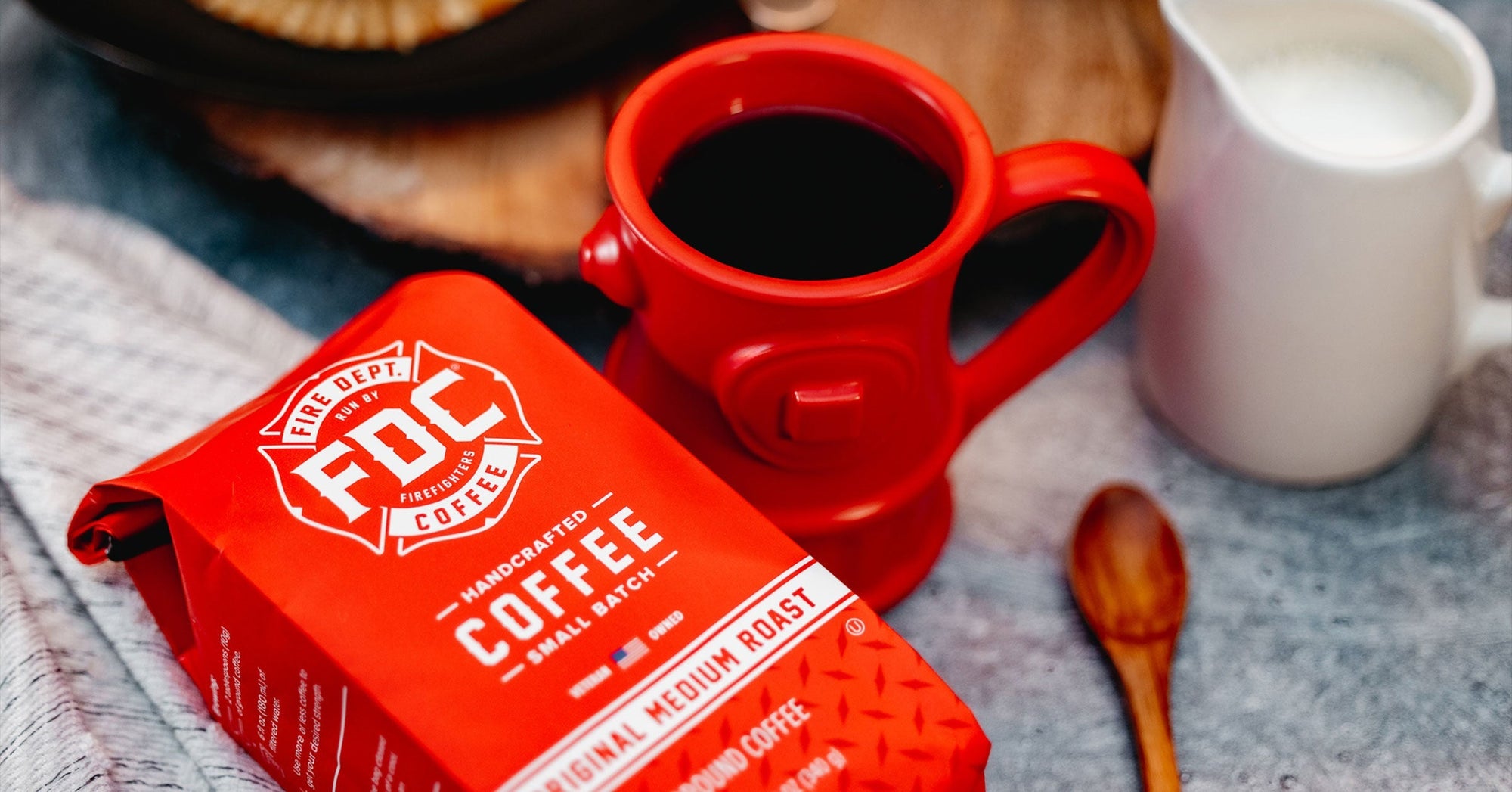 Coffee bag laying down on a table next to a fire hydrant coffee mug and wooden spoon.