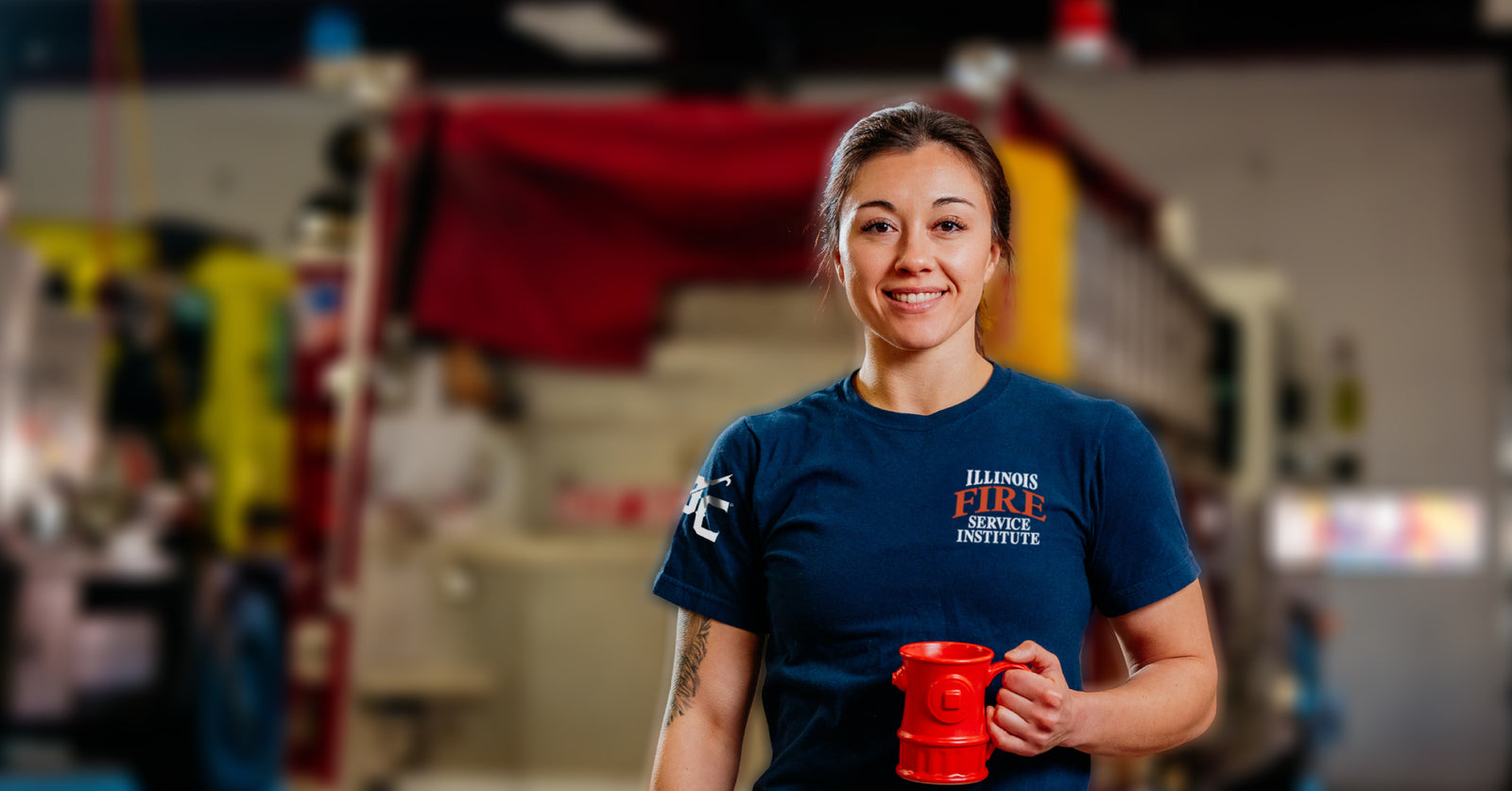Female firefighter smiling and holding a cup of coffee in a red fire hydrant shaped mug.