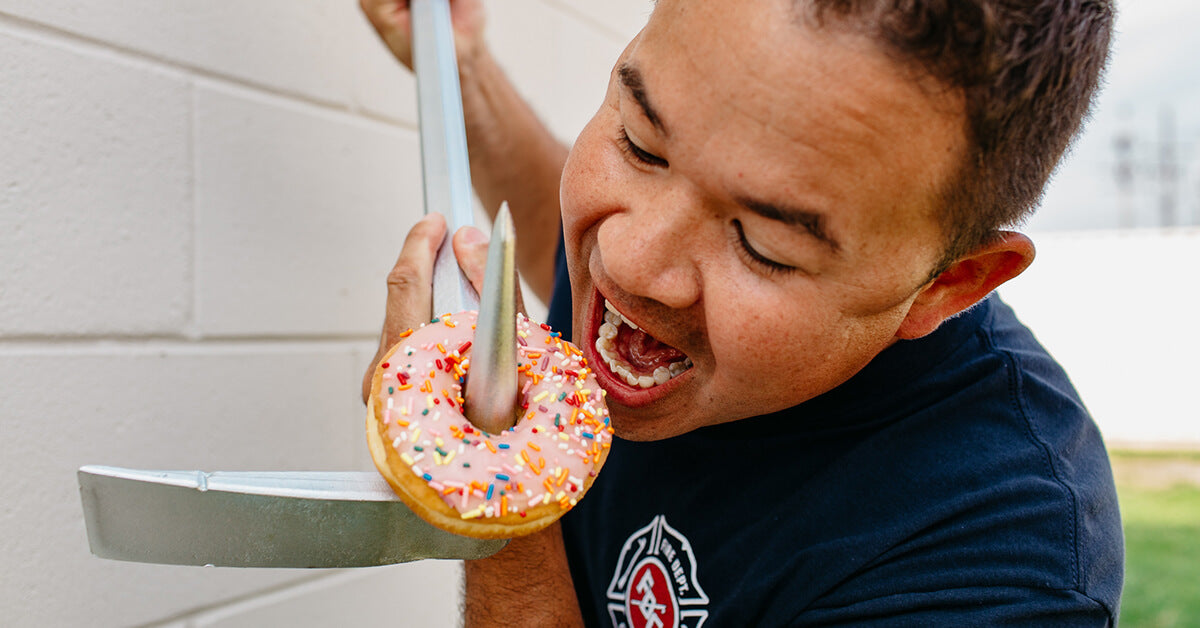 Man eating a donut off a halligan, firefighter tool.