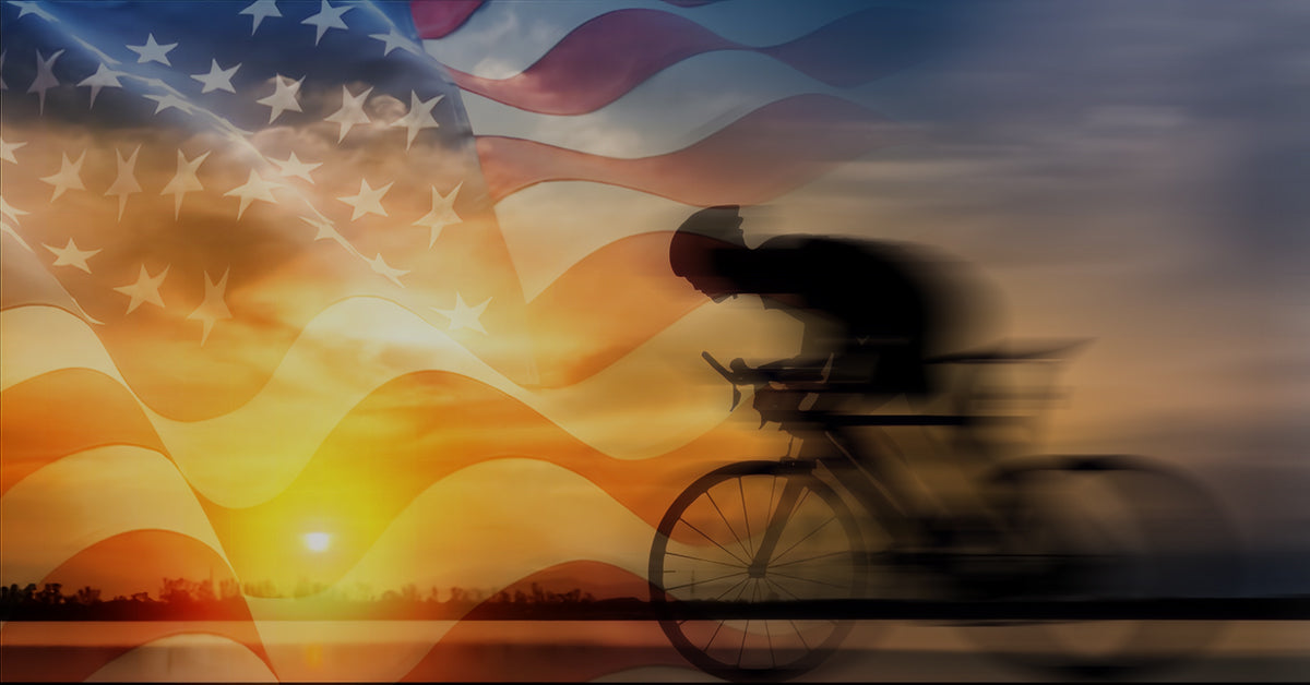 Image of a cyclist riding by a cityscape with an America flag superimposed in the background.