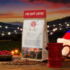 Fire Dept. Coffee package with a red mug, coffee beans, and Christmas decorations against a sunset backdrop.