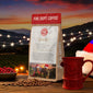 Fire Dept. Coffee package with a red mug, coffee beans, and Christmas decorations against a sunset backdrop.