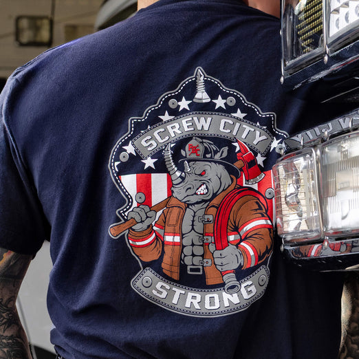 Navy blue t-shirt with a graphic design of a rhino in a firefighter helmet and American flag, with ’Screw City Strong’ text, worn by a person.

