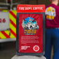 Fire Department Coffee package with a fire truck illustration and text, set against a blurred background of a fire truck and person.