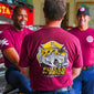 Three men wearing maroon t-shirts with a fire truck graphic and ’Fueled by Pride’ text.