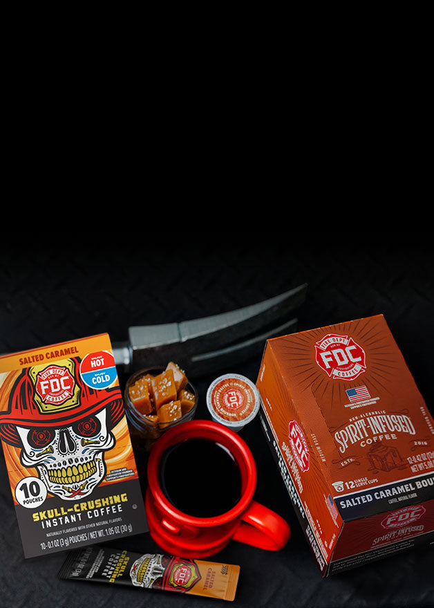 Two boxes of FDC Salted Caramel Instant Coffee with a red mug and sugar packets on a dark surface.