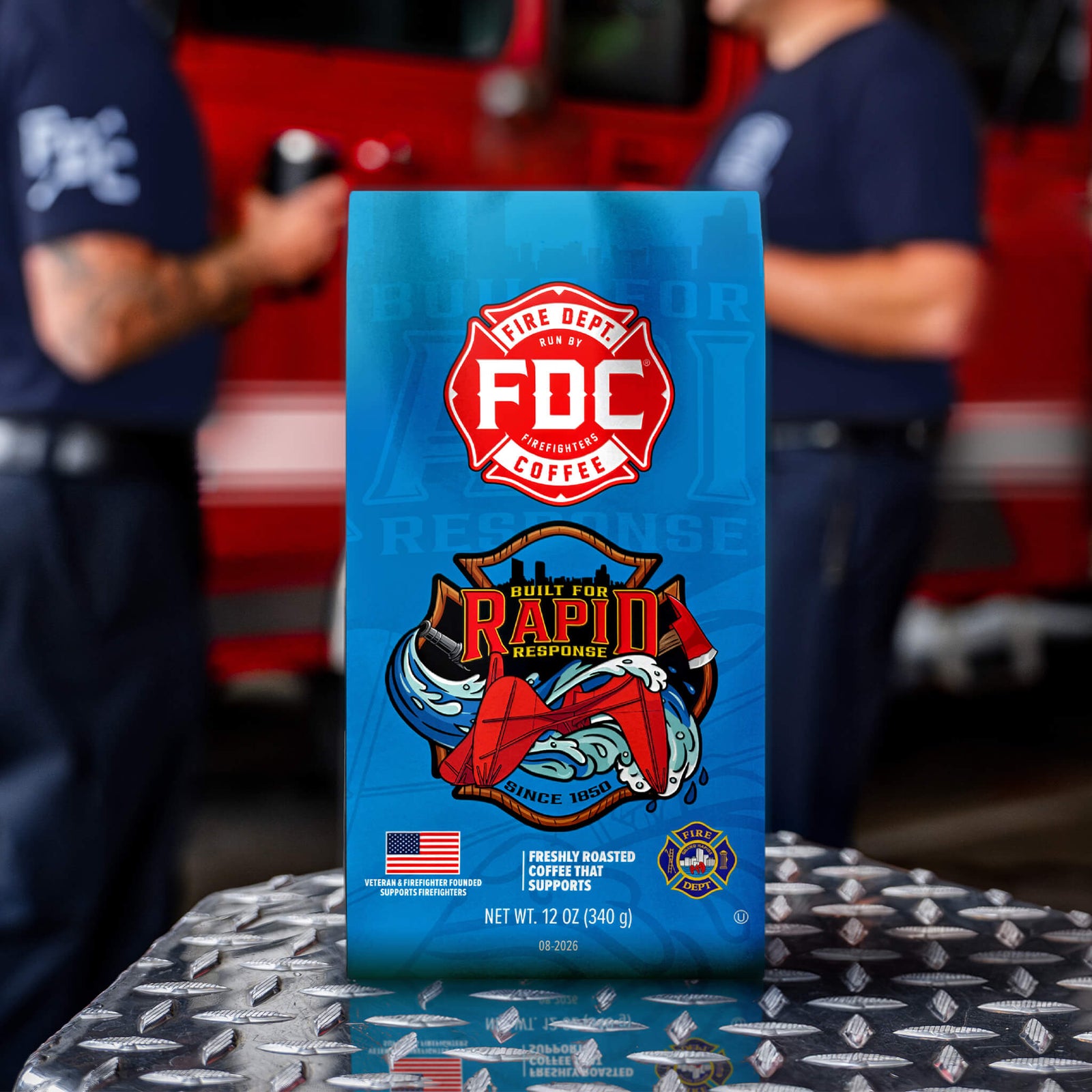A blue bag of FDC Fire Department Coffee featuring a red fire department emblem and an illustration of a fire truck and firefighter gear, with the text 'GIVES BACK TO SUPPORT' below on a black background.