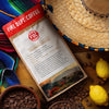 Fire Dept. Coffee package with coffee beans, lemons, and a straw hat on a wooden surface.