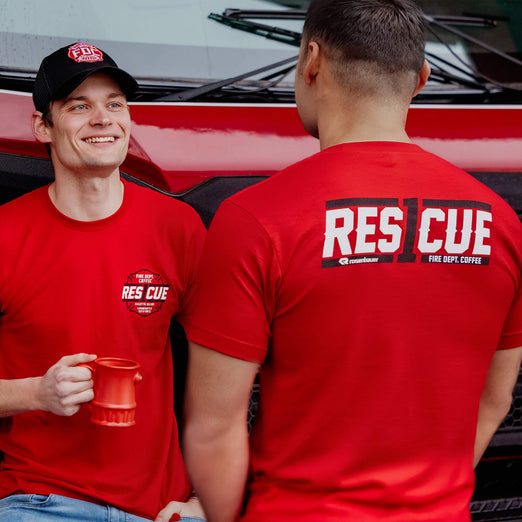Two men wearing red ’Rescue’ t-shirts with a coffee cup in front of a vehicle.