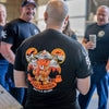 A man standing with his back to the camera wearing a black t-shirt with a large graphic on the back. The graphic features an orange fire hydrant surrounded by mountains, a bear, and the text 'FIGHT TOGETHER' and 'BATTLE AS ONE'.
