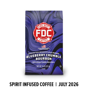 A bag of FDC Fire Department Bourbon Coffee in Blueberry Crumble Bourbon flavor, featuring a purple and blue marbled design with a red FDC logo, shown on a white background with text below reading 'SPIRIT INFUSED COFFEE | JULY 2026'.