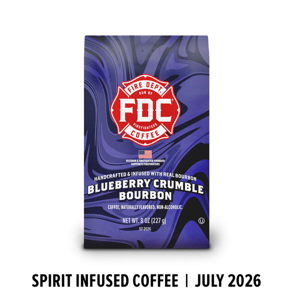 A bag of FDC Fire Department Bourbon Coffee in Blueberry Crumble Bourbon flavor, featuring a purple and blue marbled design with a red FDC logo, shown on a white background with text below reading 'SPIRIT INFUSED COFFEE | JULY 2026'.