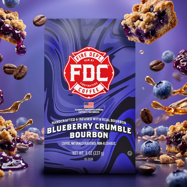 A bag of FDC Fire Department Bourbon Coffee in Blueberry Crumble Bourbon flavor, featuring a purple and blue marbled design with a red FDC logo, shown on a white background with text below reading 'SPIRIT INFUSED COFFEE | JULY 2026'.