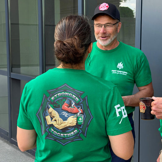 Two people wearing green shirts with a logo and text, standing outside a building.