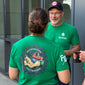 Two people wearing green shirts with a logo and text, standing outside a building.