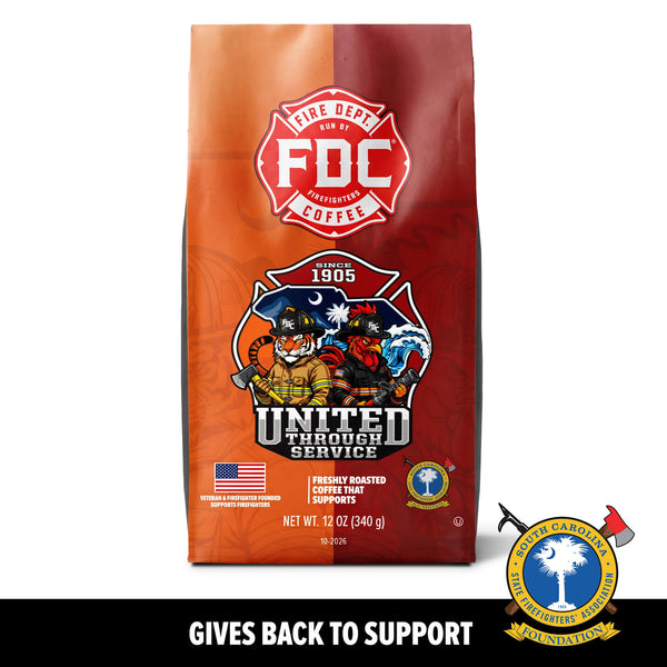 A 12 oz bag of FDC Fire Department Coffee on a white background with a black banner at the bottom reading 'GIVES BACK TO SUPPORT'. The bag is orange and red with a prominent red FDC logo and a 'United Through Service' firefighter illustration.