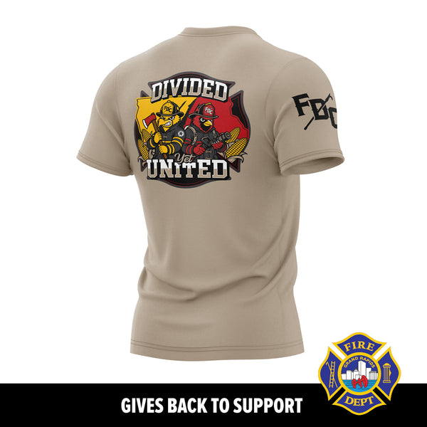 A tan short-sleeve T-shirt shown from the back on a white background, with a large firefighter-themed graphic reading 'DIVIDED BUT UNITED' and a fire department badge on the back, plus partial sleeve text. A black banner at the bottom reads 'GIVES BACK TO SUPPORT' and includes a fire department emblem.