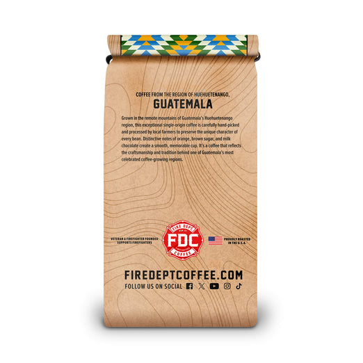 A vertical bag of Fire Dept Coffee from Guatemala, featuring a light brown wood-grain patterned design with black text and a colorful patterned ribbon at the top.