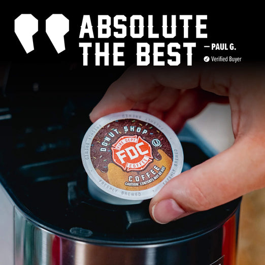 A hand inserts a round coffee K-cup pod into a coffee maker. The pod label reads ’Donut Shop FDC Coffee’ and the image includes large text at the top that says ’ABSOLUTE THE BEST’ with a quote attribution to Paul G.