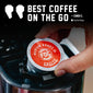 A hand inserts a single FDC Coffee Medium Roast single-serve pod into a coffee maker. The pod has a red and white label with the FDC logo.