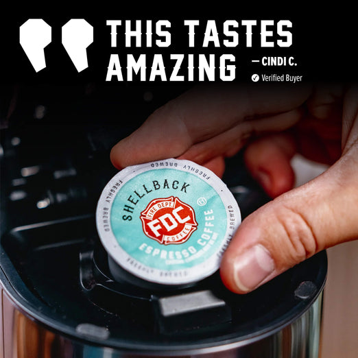 A hand inserts a round coffee capsule into a black coffee maker. The capsule label reads ’SHELLBACK’ and ’FOC Specialty Coffee’, with a large promotional text overlay at the top that says ’THIS TASTES AMAZING’ and ’CINDI C.