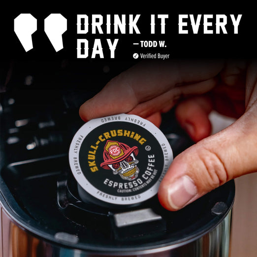 A hand inserts a single round coffee pod into a black coffee maker. The pod is branded Skull-Crushing Coffee and reads ’Espresso Coffee.