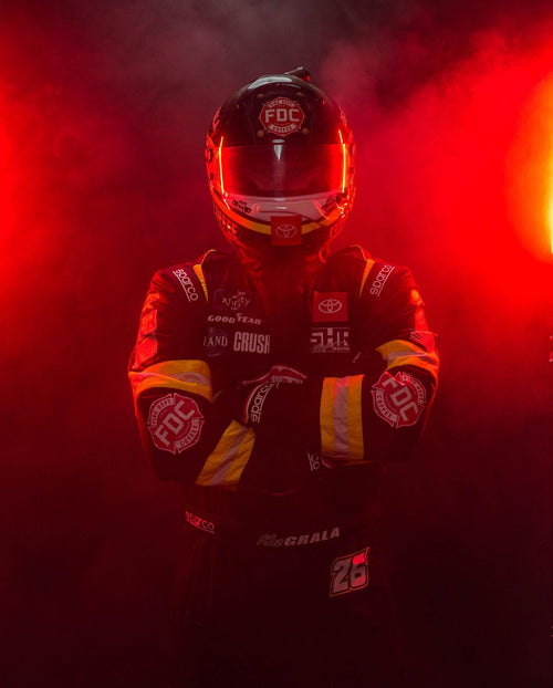 Driver Kaz Grala in racing gear with smoke around him and Fire Department Coffee logo on his gear