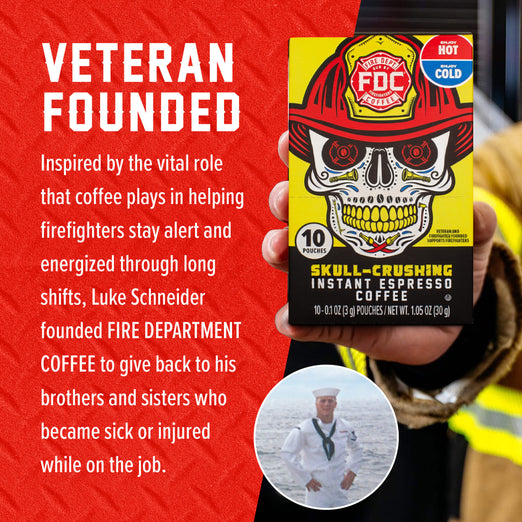 A hand holds a box of Fire Department Coffee ’Skull-Crushing’ Instant Espresso Coffee against a red textured background with white text. The box features a yellow and black design with a skull wearing a firefighter helmet.