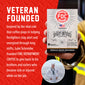 A hand holds a box of FOC Fire Department Coffee against a red promotional background with white text reading ’VETERAN FOUNDED’ and a circular inset photo of the founder in a sailor uniform.
