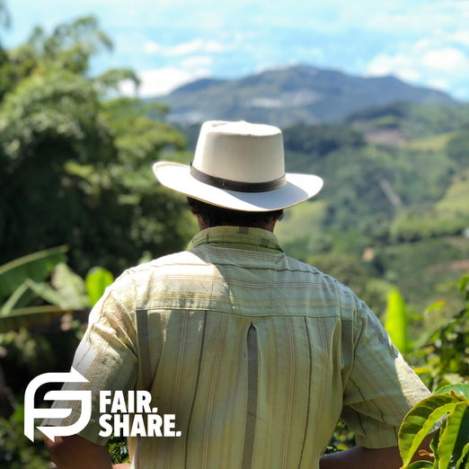 A photo of a coffee farmer looking out at his yield with the words, ”Fair. Share” in the bottom left corner.