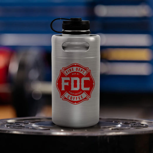 Lifestyle photo featuring a 64oz silver stainless steel Fire Department Coffee Growler with Fire Department Coffee logo facing forward. 