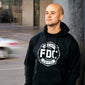 A lifestyle image of someone wearing a Fire Department Coffee Black Hoodie. The front of the hoodie has a white FDC maltese cross on it.