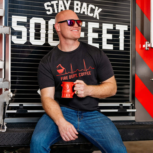 Five Fire Dept. Coffee EKG T-shirts displayed in purple, vintage white, pink, black, and heather gray, each featuring a coffee pot pouring into a heartbeat line with “Fire Dept. Coffee” text underneath.