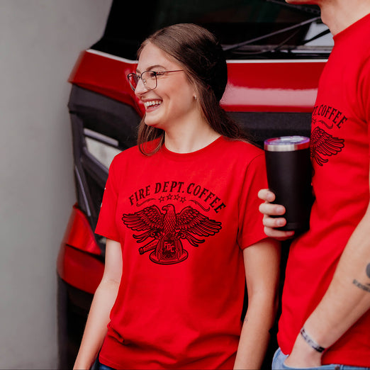 Two people wearing red ’Fire Dept. Coffee’ t-shirts with a coffee cup in front of a red fire truck.