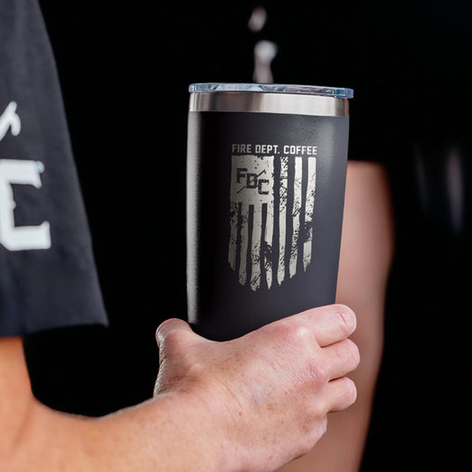 Person holding a black tumbler with FDC Flag design, against a dark background