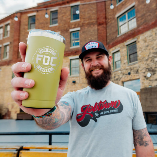 A man holding a 20 ounce green tumbler that has an FDC maltese cross logo engraved on the front