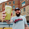 A man holding a 20 ounce green tumbler that has an FDC maltese cross logo engraved on the front