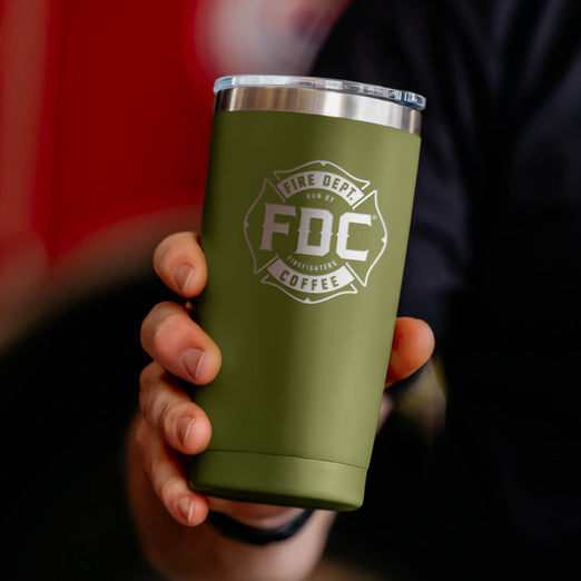 A person holding a green tumbler with the Fire Department Coffee logo, against a dark background.