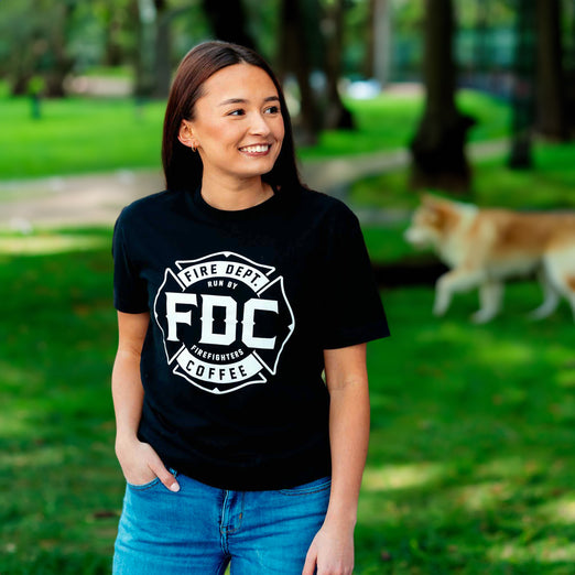 A lifestyle image of someone wearing the Fire Department Coffee Black Shirt. The front of the shirt features the FDC maltese cross logo in white.