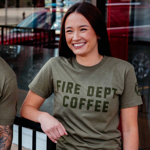 A lifestyle image of someone wearing the FDC Military Green Shirt. The front of the shirt says ”Fire Dept. Coffee” in dark green lettering.