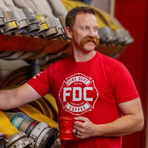 A red Fire Department Coffee T Shirt, featuring FDC's maltese cross logo in white.