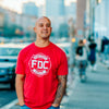 A lifestyle image of someone wearing the Fire Department Coffee Red Shirt. The front of the shirt features the FDC maltese cross logo in white.