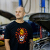 Someone wearing the black Skull Shirt with a skull wearing an FDC fire helmet surrounded by flames in the center. Around the skull is text that reads "Fire Department Coffee".