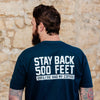 A lifestyle image of someone wearing the Stay Back Shirt in Navy. The back of the shirts reads, "Stay back 500 feet until I've had my coffee" in white
