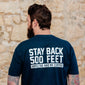 A lifestyle image of someone wearing the Stay Back Shirt in Navy. The back of the shirts reads, ”Stay back 500 feet until I’ve had my coffee” in white