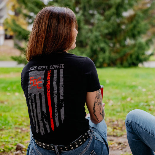 A lifestyle image of someone wearing the Thin Red Line Shirt. The back of the shirt features the thin red line flag with the FDC pike pole logo and text that reads ”Fire Dept. Coffee”