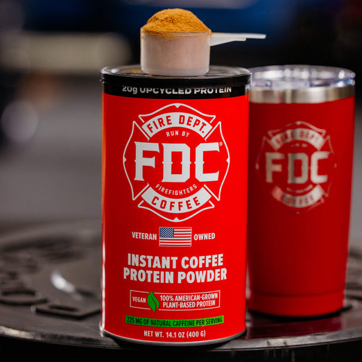A can of Fire Dept. Coffee’s Instant Coffee Protein Powder next to a Red FDC Tumbler.